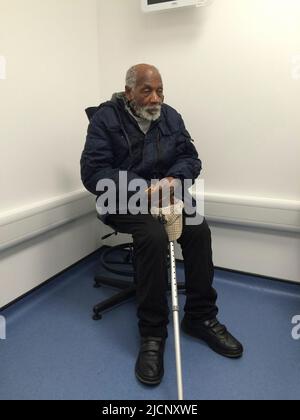 Elderly man sitting down in a hospital waiting room, holding a biscuit in his hands. Stock Photo