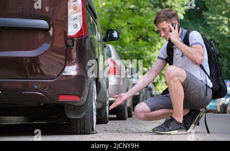 Driver calling road service for assistance having vehicle trouble with punctured flat tire on car parked on roadside Stock Photo