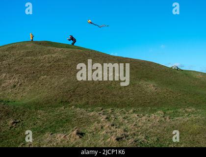 Wiltshire,England,UK-February 18th 2021: A little boy watches his Dad running along the top of the windswept Neolithic long barrow,dragging a kite hel Stock Photo