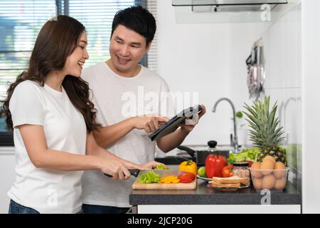couple cooking and preparing vegetables according to a recipe on a tablet computer in the kitchen at home Stock Photo