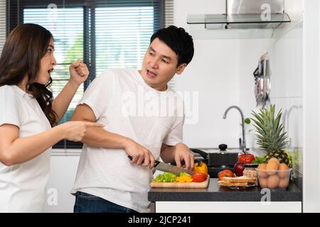 stressed young couple conflict in their kitchen, angry woman pointing hand to man for preparing vegetables healthy food Stock Photo