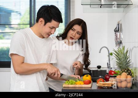 tired couple cooking and preparing vegetables  in the kitchen at home, angry woman pointing hand to man Stock Photo