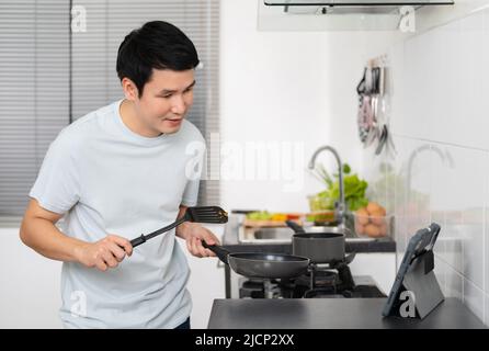 young vlogger man making video call from digital tablet while cooking in the kitchen at home Stock Photo
