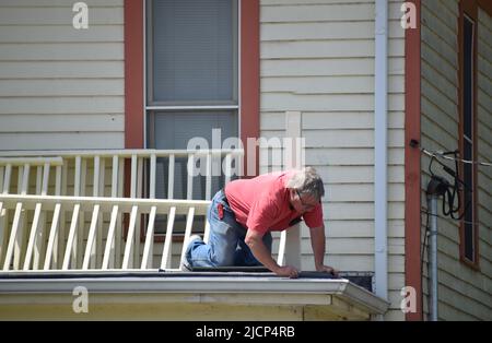 A handyman kneeling on and working on a roof of a house Stock Photo