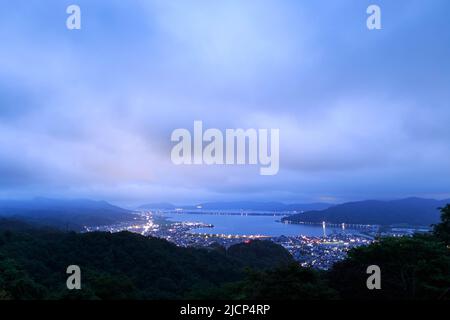 Last glow of sunset hits clouds over small city on coast at blue hour Stock Photo