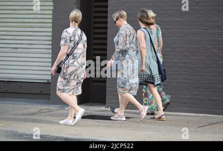 Four women walking down a city side walk, three women wearing long dresses Stock Photo