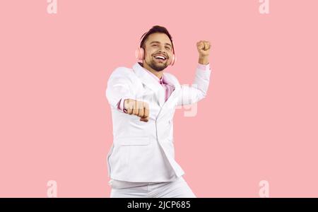 Funny man in suit having fun listening to music in wireless headphones on colored background. Stock Photo