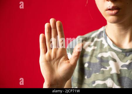 Hand of a girl in a camouflage uniform on an isolated red background close-up, hand gesture,stop Stock Photo