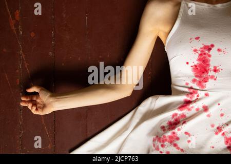 A murdered and tortured Ukrainian woman in a white dress and bloodstains lies on the floor of the house, a protest action by Ukrainian women, protecti Stock Photo