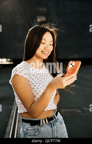 Young Asian woman smiling while using her mobile phone on the street. Stock Photo