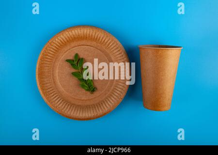 Disposable paper biodegradable cup, plate and green leaf on a blue background. Top view. Flat lay composition. Stock Photo
