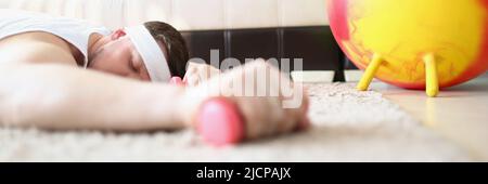 Tired man laying on carpet floor with dumbbell equipment in hand Stock Photo