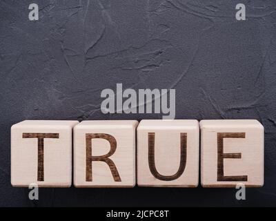 Text TRUE on wooden cubes on grey concrete background Stock Photo