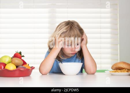 Portrait of kid with no appetite. Concept of loss of appetite. Kid preteen boy in the kitchen at the table eating vegetable and fruits during the Stock Photo