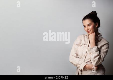 Portrait of emotive good-looking woman smiling while looking aside and standing against gray background Stock Photo
