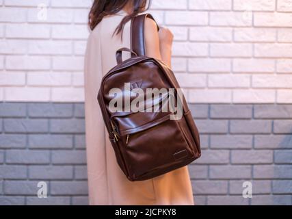 Woman holding brown leather backpack in the hand on the brick wall background. Unisex bag Stock Photo