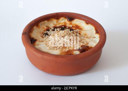 Profile view of tasty baked rice pudding with hazelnuts on, traditional dessert known as in Turkish "sutlac" in earthenware casserole, isolated white Stock Photo