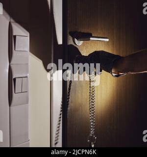Man hand in a black glove opens the office door in the night light of a flashlight Stock Photo