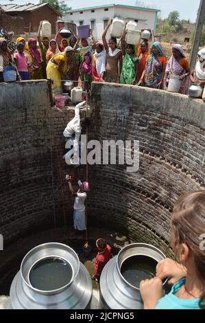 Indian people of an aboriginal 'Kol' community refill drinking water in steel and plastic containers from a well , in Nawargawa Village, Madhya Prades Stock Photo