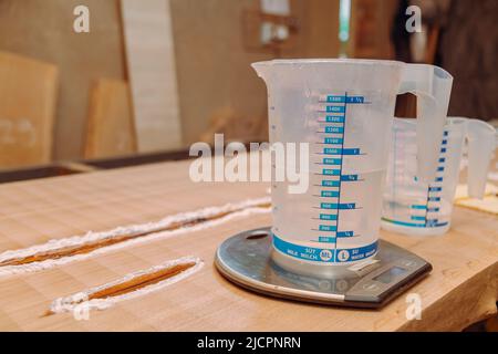 Liquid cup with epoxy resin on scales. Process of making a craft resin and wood table Stock Photo