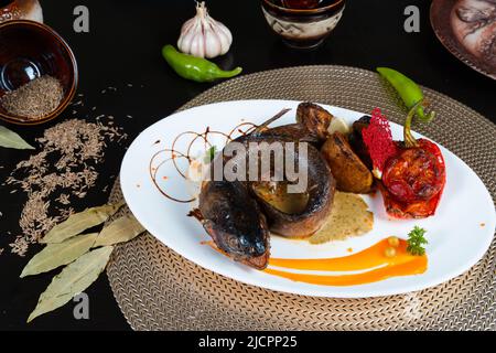 White plate with grilled trout with potato, red pepper, tomato and lemon on a black background Stock Photo