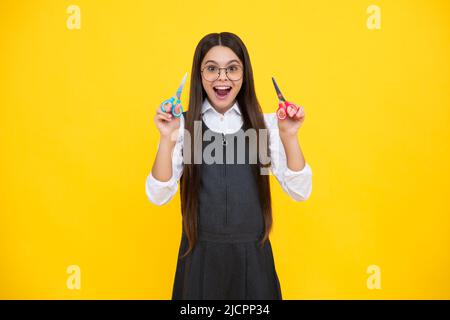 Excited amazed teenage girl with scissors, isolated on yellow background. Child creativity, arts and crafts. Stock Photo