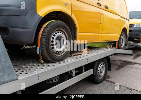 White small cargo truck car carrier loaded with two yellow van minibus on flatbed platform and semi trailer tow on roadside highway road. Volunteer Stock Photo