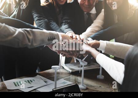 Group of businesspeople join hands over renewable wind energy project to celebrate team success - business and sustainability lifestyle concept. Stock Photo