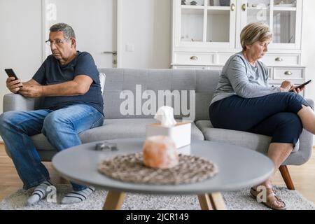 Senior couple sitting on couch and using their mobile phones at home Stock Photo