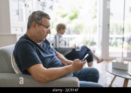 Senior couple sitting on couch and using their mobile phones at home Stock Photo