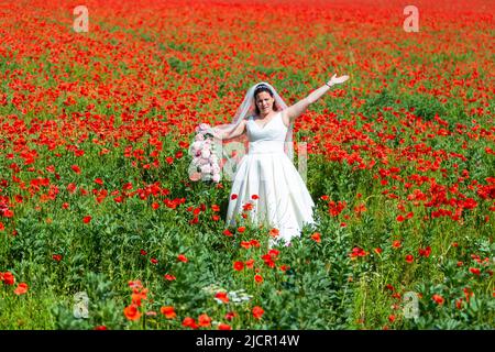 Bride in white wedding dress in a poppy field, UK 2022 Stock Photo