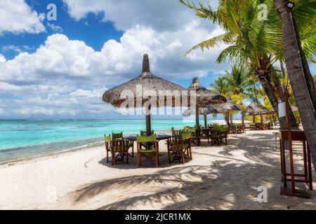 Beach cafe on sandy beach under straw umbrella, palm trees and beautiful sea on exotic tropical island. Stock Photo