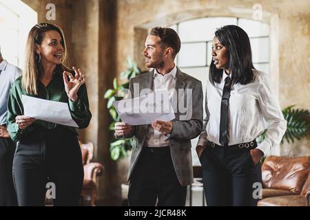 Three cheerful businessperson walking together in an office. Diverse group of businesswomen smiling while having a discussion. Successful colleagues c Stock Photo