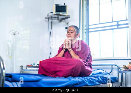 Senior woman in operation gown at hospital praying god by joining hands - concept of healthcare, medical treatmet and hope Stock Photo