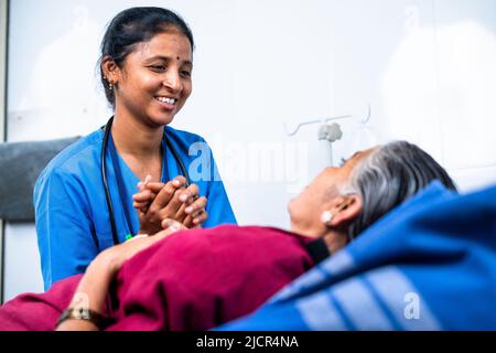 happy smiling Nurse consoling elderly senior patient aftrer surgery at hsopital on bed - concept of caring, medical treatment and healthcare service Stock Photo