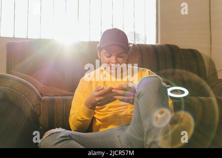 Cybersport pro Hispanic gamer. Winning video game on mobile. Young man sitting in a chair with a smartphone in the living room Stock Photo