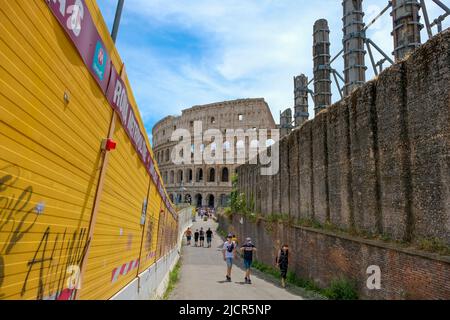 Rome, Italy - June 6, 2022: Tourists walk to and from the ancient Colosseum along a yellow wall made with modern construction techiniques and material Stock Photo