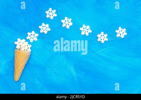 Ice cream waffle cone and white snowflakes arranged on a blue textured background with copy space. Stock Photo