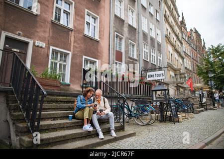 Happy senior couple tourists sitting on stairs and having take away coffee outdoors in town Stock Photo
