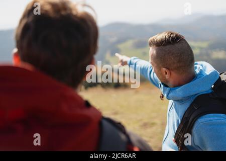 Two paragliders men standing on the top of mountain, looking at view and pointing. Stock Photo