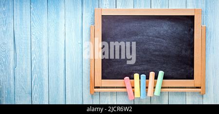 Small black board with colored chalks on blue wooden planks. Back to school concept Stock Photo