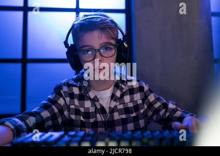 Young gamer boy with headphones playing computer video game. Stock Photo