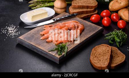 Beautiful delicious red fish slices on a wooden cutting board against a dark concrete background Stock Photo