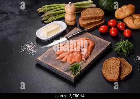 Beautiful delicious red fish slices on a wooden cutting board against a dark concrete background Stock Photo