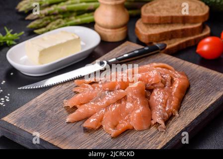 Beautiful delicious red fish slices on a wooden cutting board against a dark concrete background Stock Photo