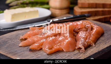 Beautiful delicious red fish slices on a wooden cutting board against a dark concrete background Stock Photo