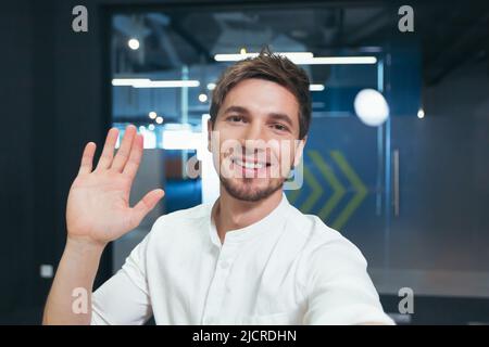 A young businessman in a shirt and beard looks into the camera of a smartphone talking happily on a video call, uses an application for video communic Stock Photo