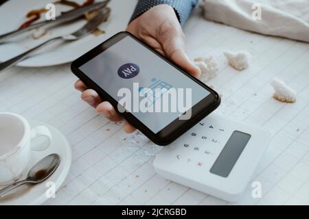 a man pays the bill at the restaurant by his mobile phone through a wireless payment terminal, placed on the table, set with a white tablecloth Stock Photo