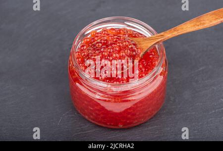 Wooden spoon with red caviar in a glass jar with caviar. Copy space. Stock Photo