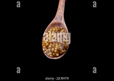 Wooden spoon full of french mustard isolated on black background. Mustard sauce made from white and black mustard seeds. Copy space. Stock Photo